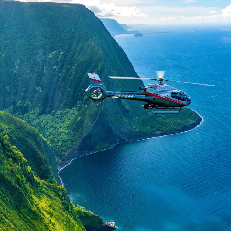 A Maverick Helicopter flying over the lushed sea cliffs in Hawaii
