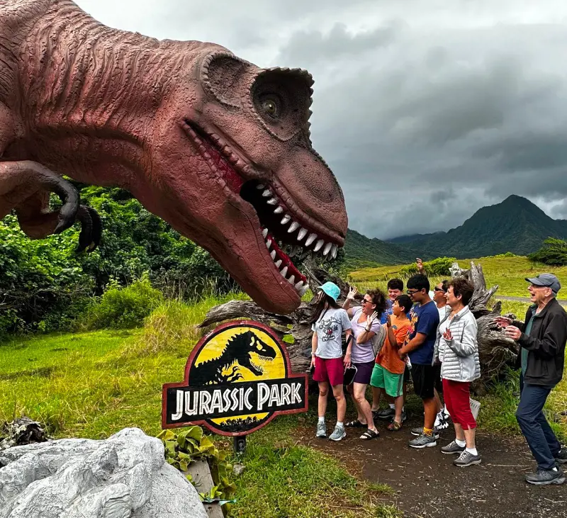 A group of visitors posing beside a Dinosaur statue at Kualoa Ranch