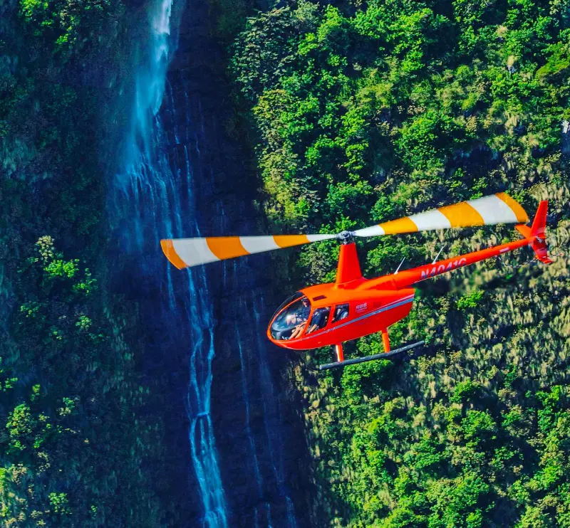 A chopper from Mauna Loa Helicopter Tours flying by an amazing waterfall in Big Island, Hawaii