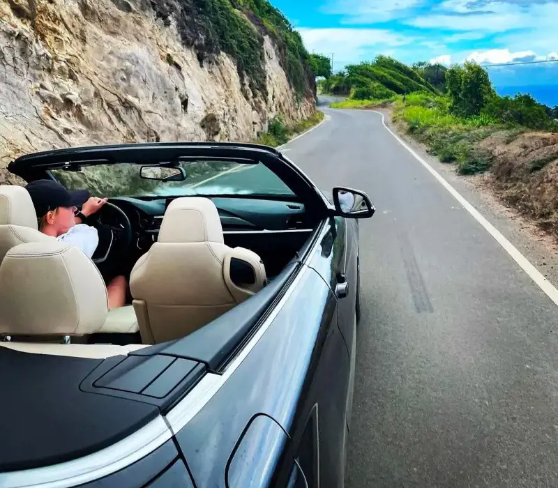 A person driving down a scenic route in a rented convertible in Hawaii