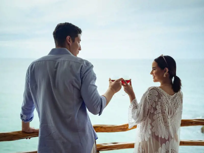 A man and a woman toasting their drinks while soaking the ocean view