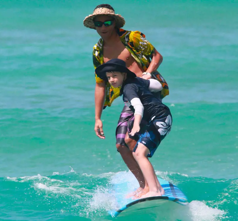 A kid learning honing his surfing skills in the Hawaiian waters with the help of his instructor