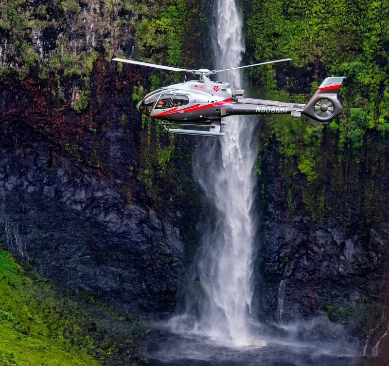 A passenger chopper from Maverick Helicopters flying past a waterfall in Hawaii