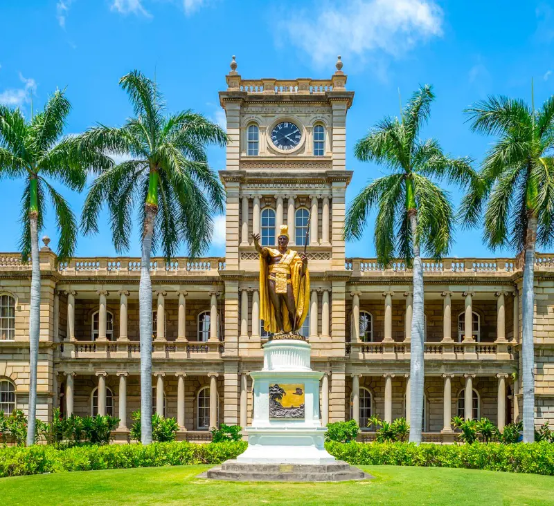 An amazing view of the Iolani Palace with the statue of King Kamehameha in the garden