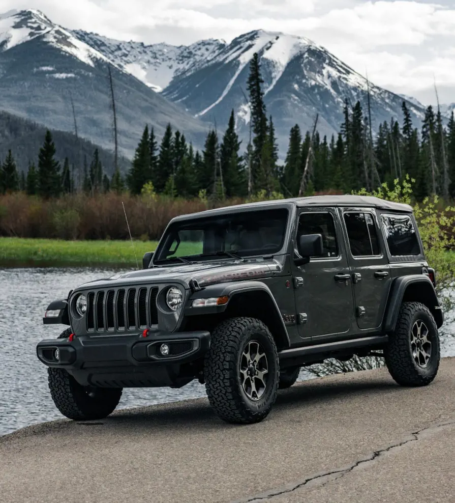 A Jeep Wrangler from the Hertz Car Rental parked on a lakeside in an exotic location