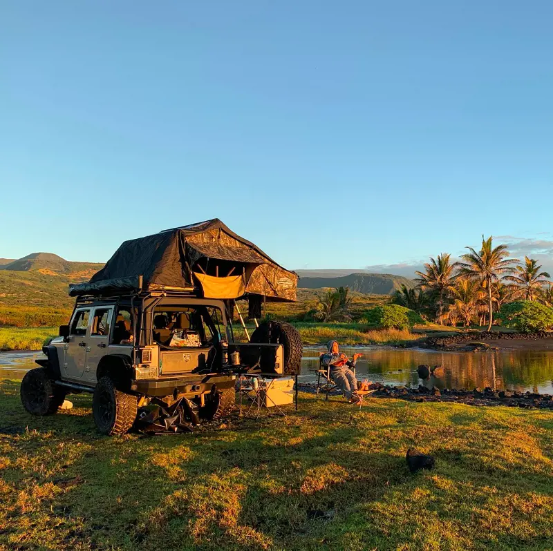 A traveler camps by the lake besides his rented SUV