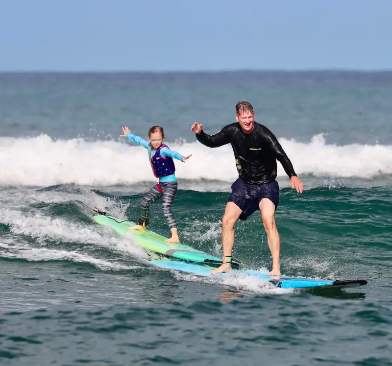 Dad and daughter surfing together at Haleiwa during the Super Surf Session in 2022