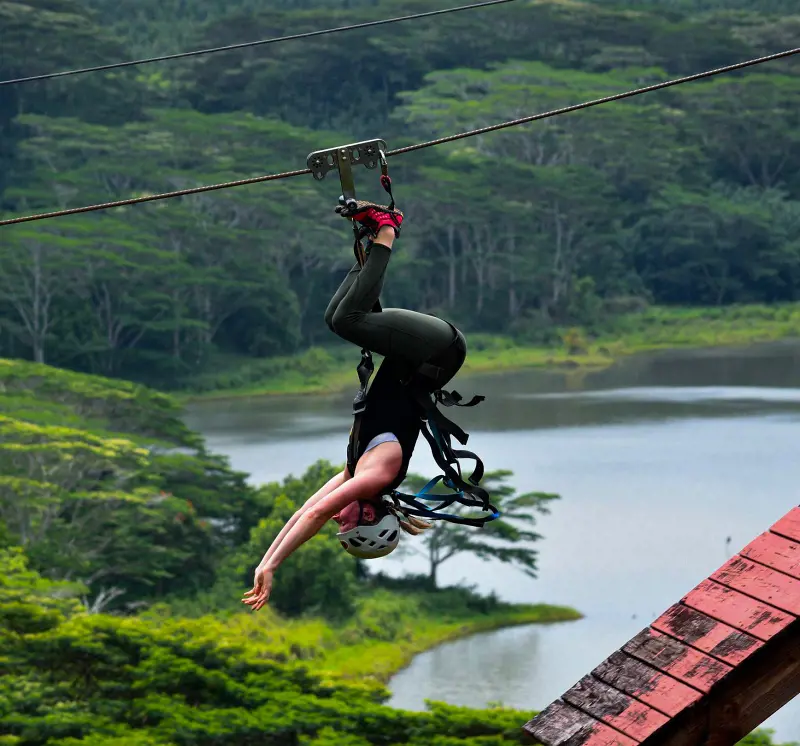 A traveler doing a hands-free stunt while ziplining in Koloa