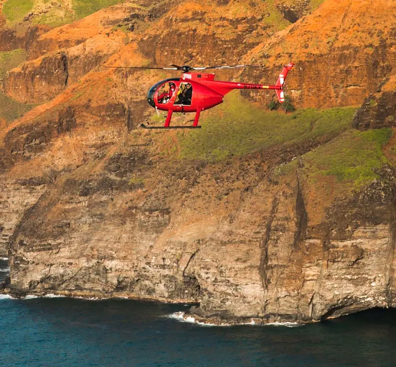 A passenger chopper from Airborne Aviation Tours flying above the cliff in Hawaii