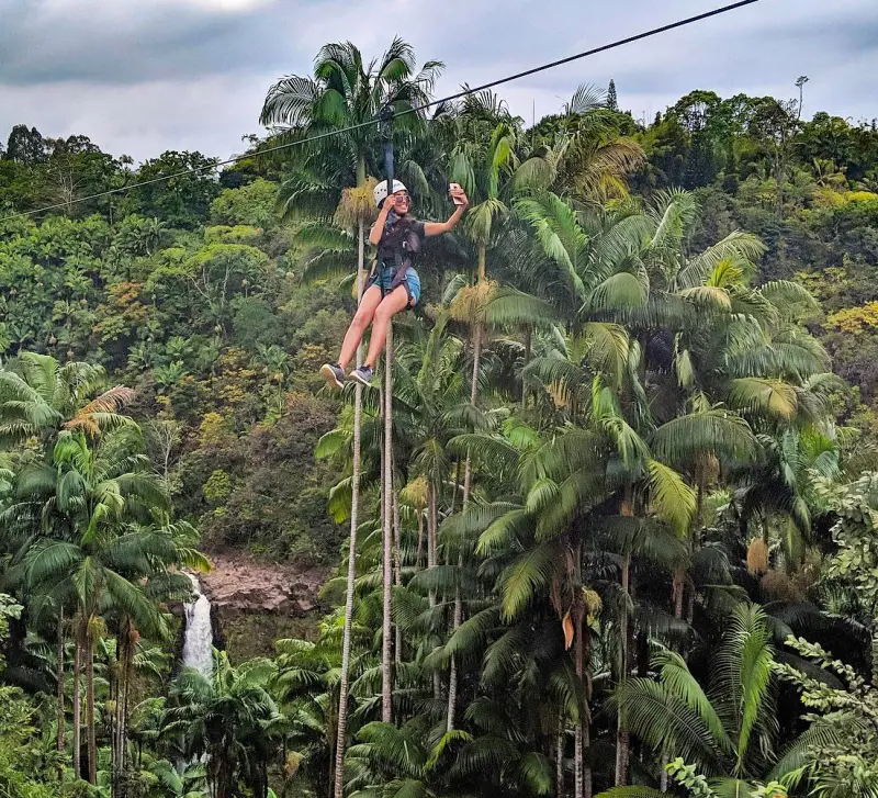 A person takes selfie while gliding on a zipline over the Hawaiian rainforest