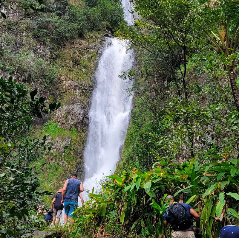 Travelers taking a hike to the base of the 250-foot-tall Mo'oula Falls in Molokai