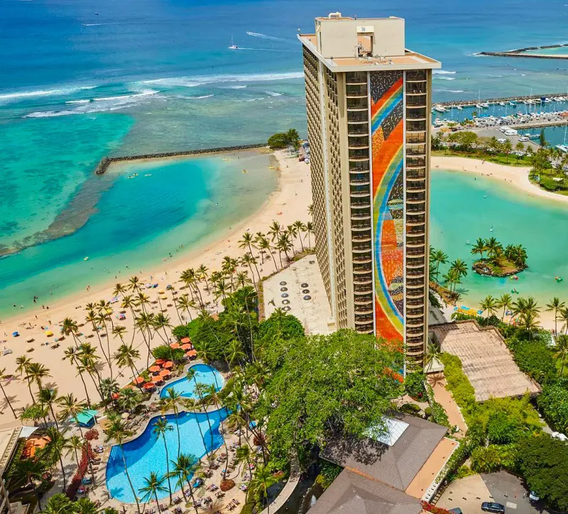 The tall-rising building of Hilton Hawaiian Village Waikiki Beach Resort and its outdoor pool by the beach
